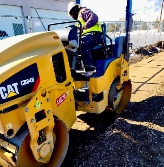 A man in yellow jacket operating a road roller.